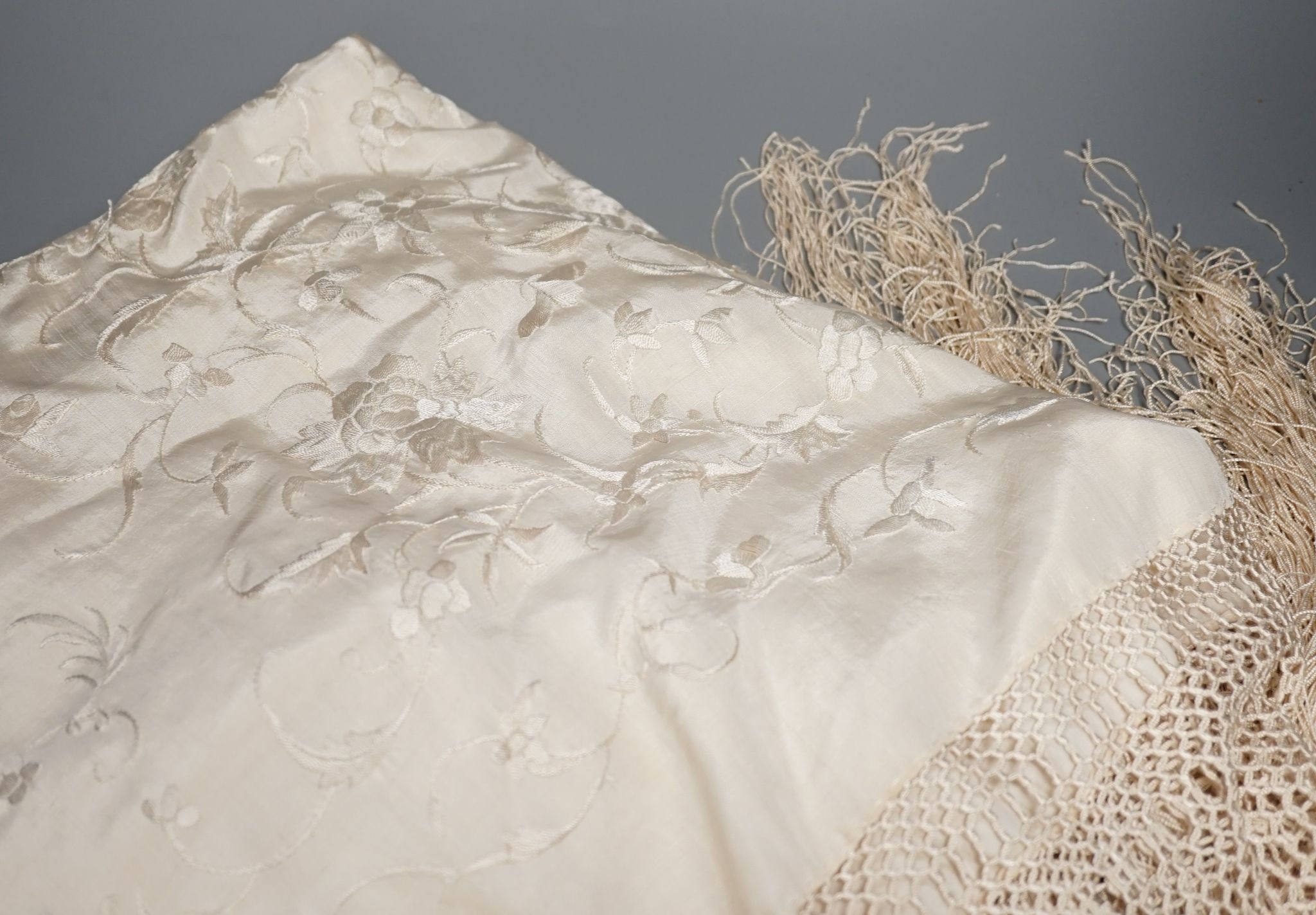A Chinese cream on cream silk, embroidered shawl with a tasselled fringed edge, 160 cms wide x 160 square.